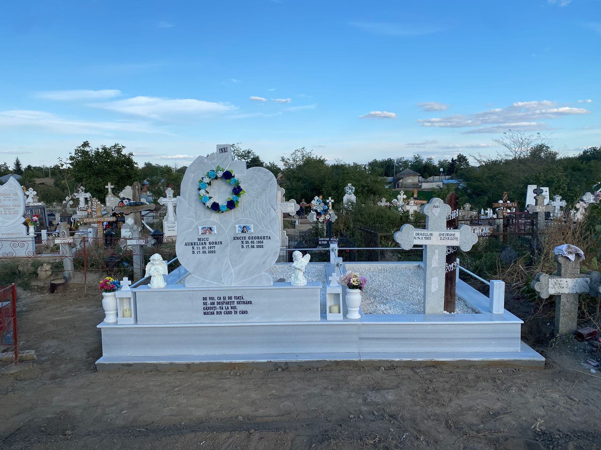 Monument din marmură albă sculptat cu aripi, cu bordură și pietriș